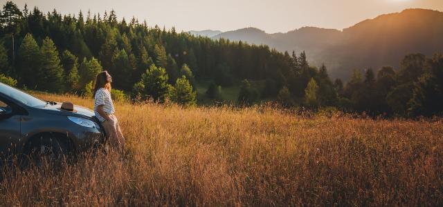 Young beautiful woman traveler enjoying the sunset in the mountains while traveling by car